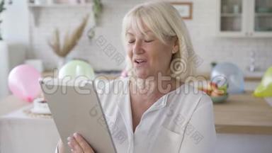 积极成熟的女人看着平板电脑，微笑着站在现代厨房。 <strong>生日庆典</strong>